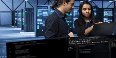 Software developers in data center running system diagnostic tests Software developers in data center running system diagnostic tests on laptop to fix problems. IT staff members deploying and error checking utilities on notebook to fix network issues performance